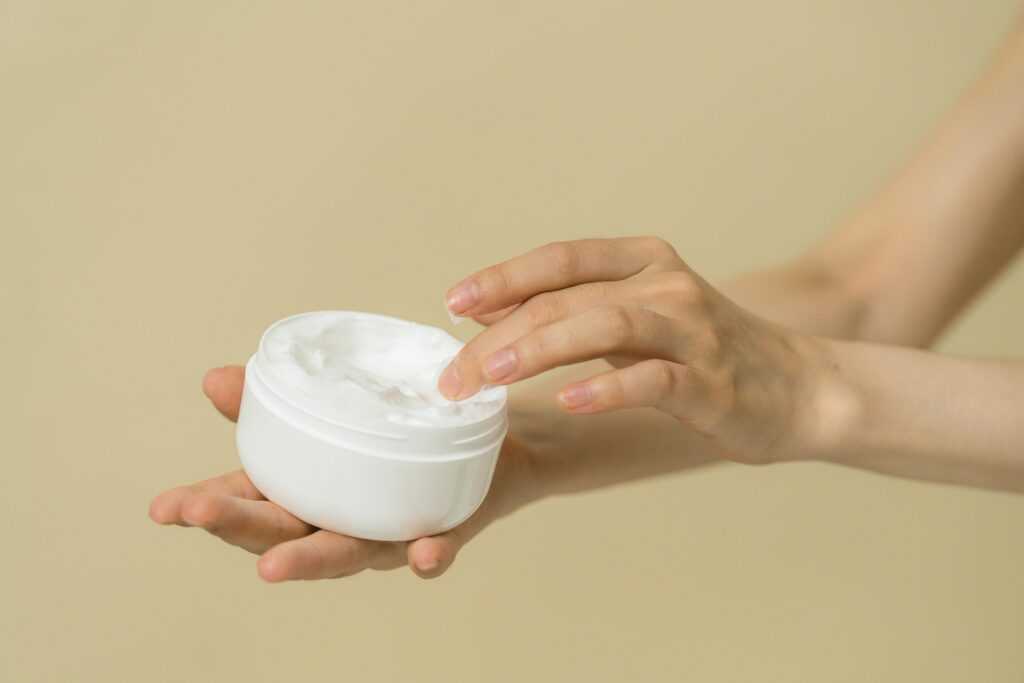 Close-up of female hands applying moisturizer from an open jar, highlighting skincare and self-care routine.